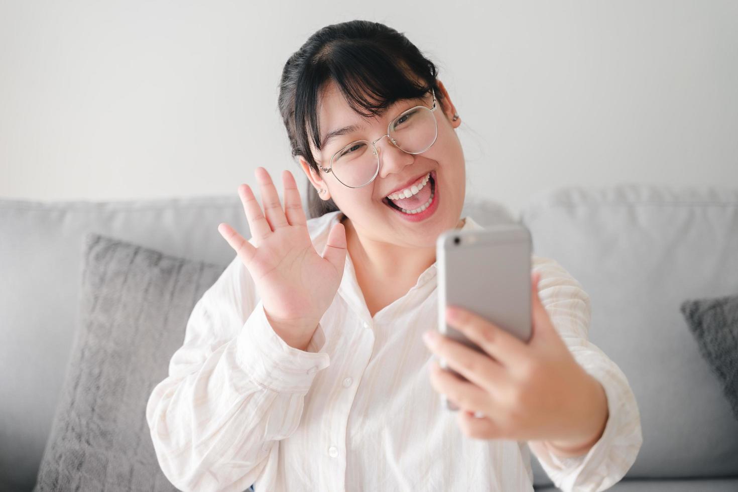 giovane donna asiatica che utilizza lo smartphone per la videoconferenza online con gli amici che agitano la mano facendo un gesto di saluto foto