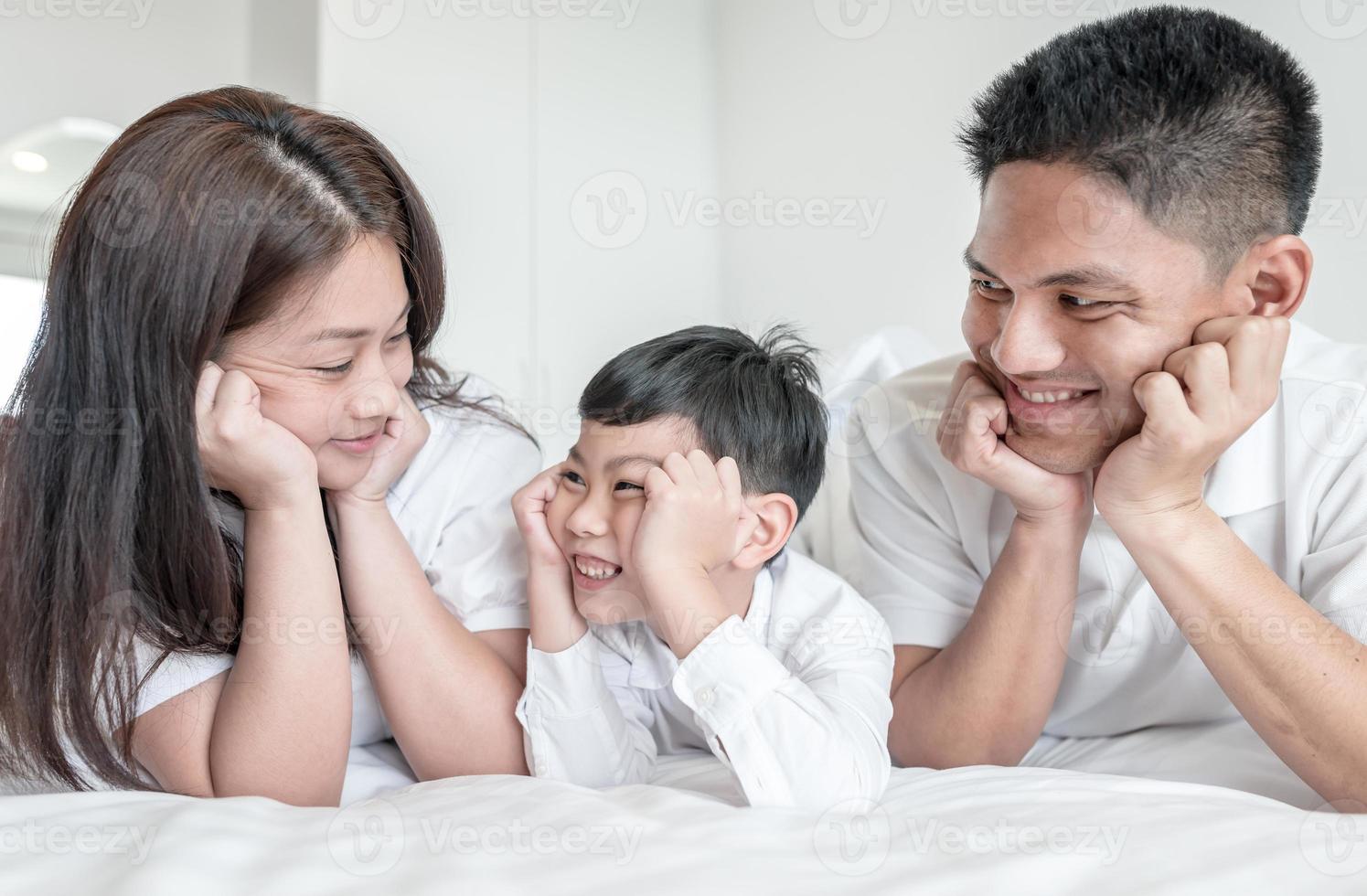 ritratto famiglia felice mamma papà e figlio sorridenti in camera da letto. guardatevi l'un l'altro. foto