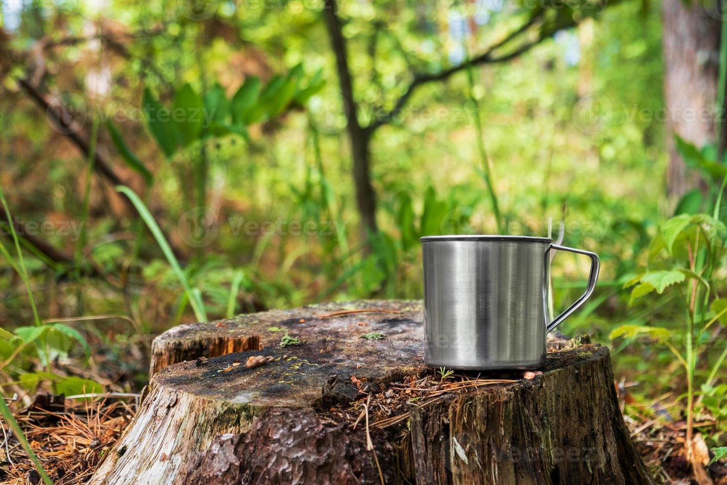 tazza turistica in metallo con bevanda calda si trova sul ceppo nella foresta. foto