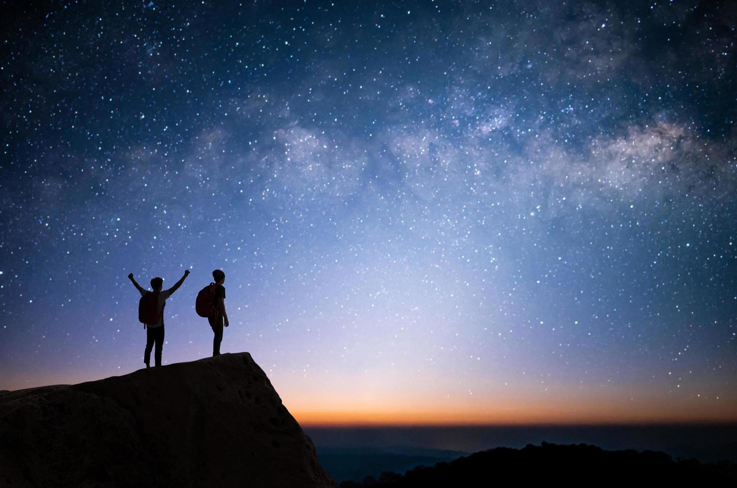 silhouette di due giovani in piedi, a braccia aperte e guardava la stella, la via lattea e il cielo notturno in cima alla montagna. si sono divertiti a viaggiare e ha avuto successo quando ha raggiunto la vetta. foto