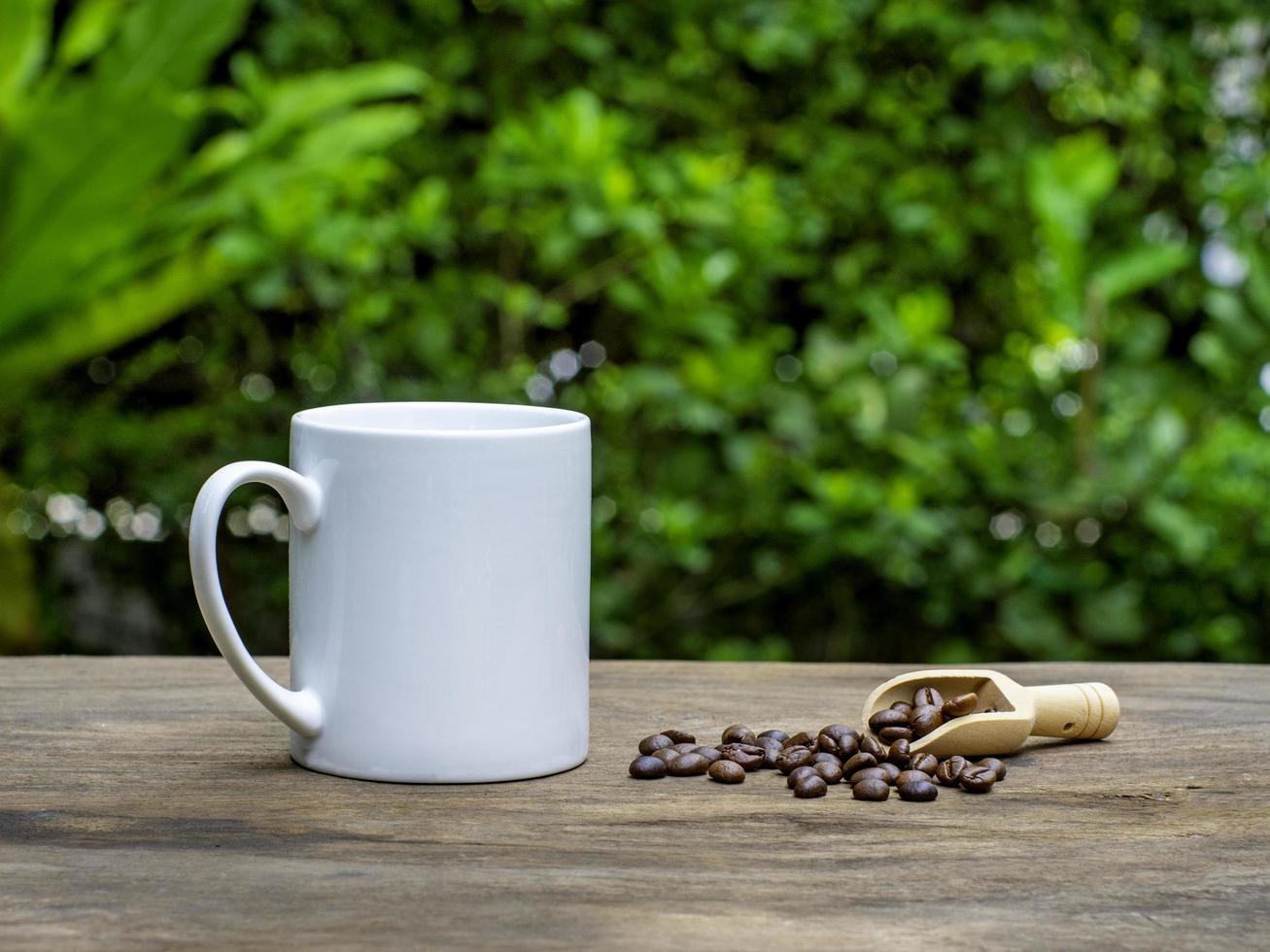 Tazza da caffè in ceramica bianca su un vecchio tavolo di legno con sfondo di alberi di bosco di chicchi di caffè tostati. effetto di messa a fuoco morbida. foto