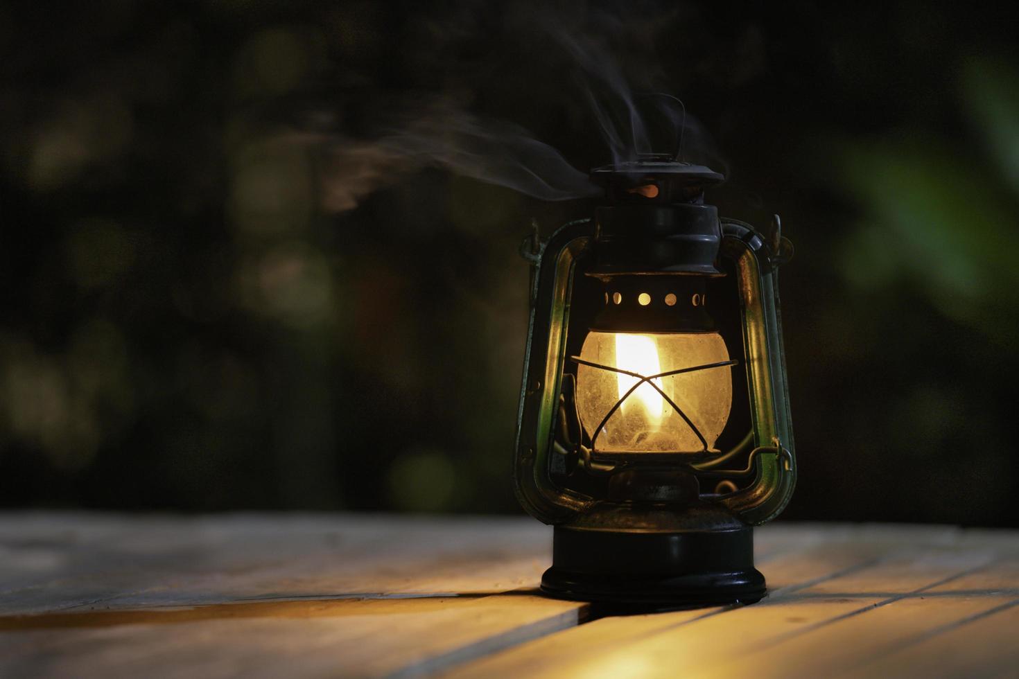 antica lampada a cherosene con luci sul pavimento in legno di notte foto