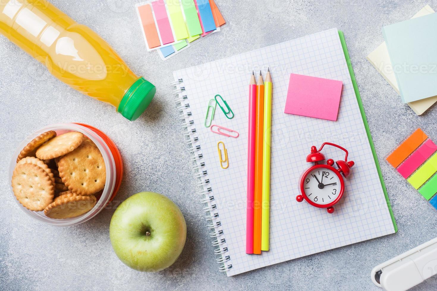 materiale scolastico e cracker per la colazione, succo d'arancia e mela fresca sul tavolo grigio con spazio per la copia. scuola di concetto. foto