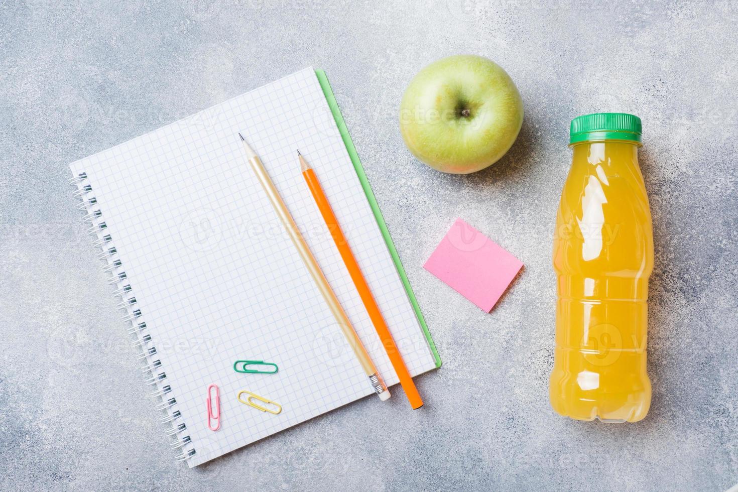 materiale scolastico e cracker per la colazione, succo d'arancia e mela fresca sul tavolo grigio con spazio per la copia. scuola di concetto. foto