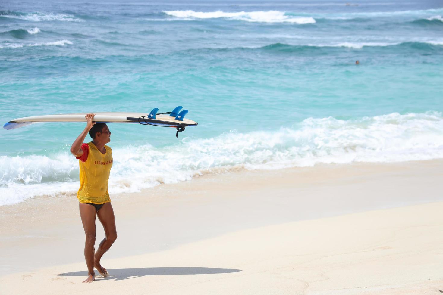 bali, indonesia 22 novembre 2021 bagnino che osserva la situazione sul mare mentre porta una tavola da surf foto