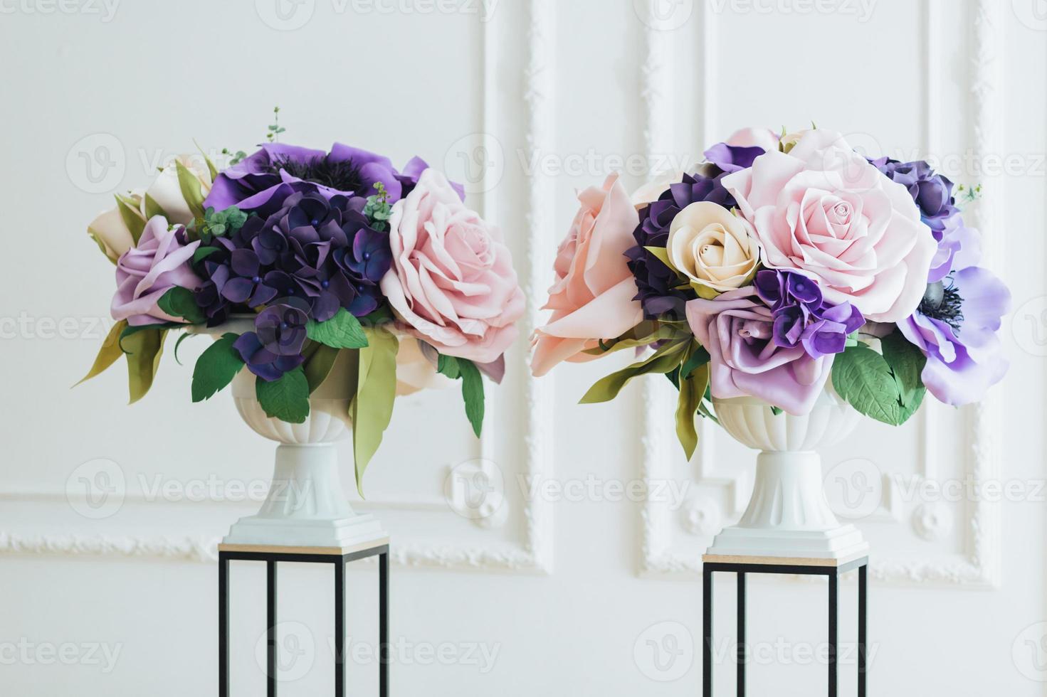 vista orizzontale di bellissimi fiori artificiali nei colori rosa e viola in vasi bianchi su supporti nella sala per la cerimonia di matrimonio. decorazione floreale foto