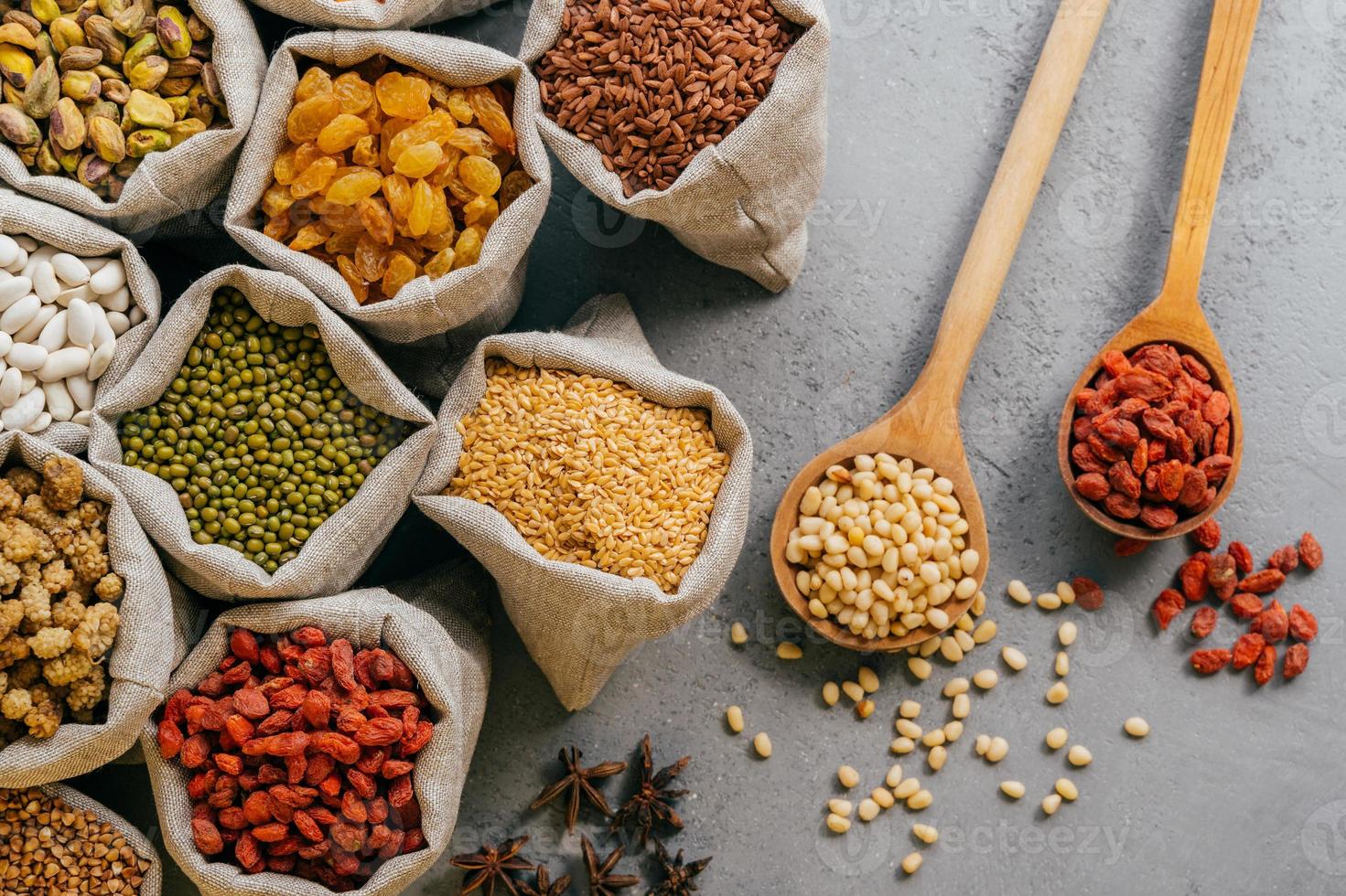 sacchi con frutta secca varia e cereali confezionati. due cucchiai di legno su sfondo grigio. legumi e cereali sani foto