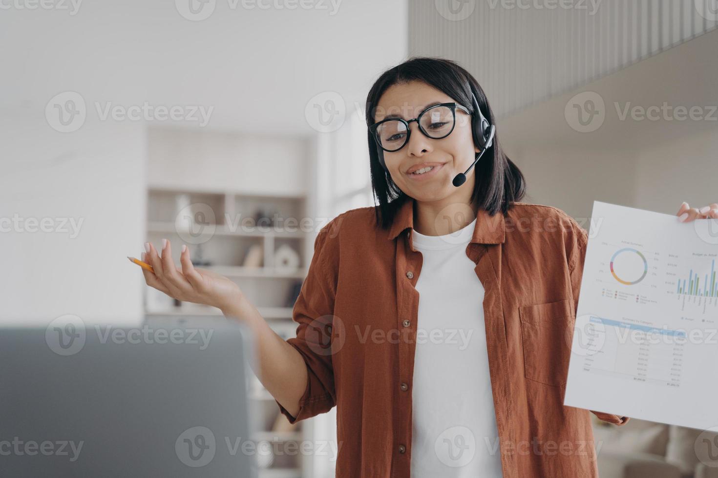 donna d'affari in occhiali, auricolare, discutere il progetto aziendale online tramite videochiamata che mostra un'infografica foto