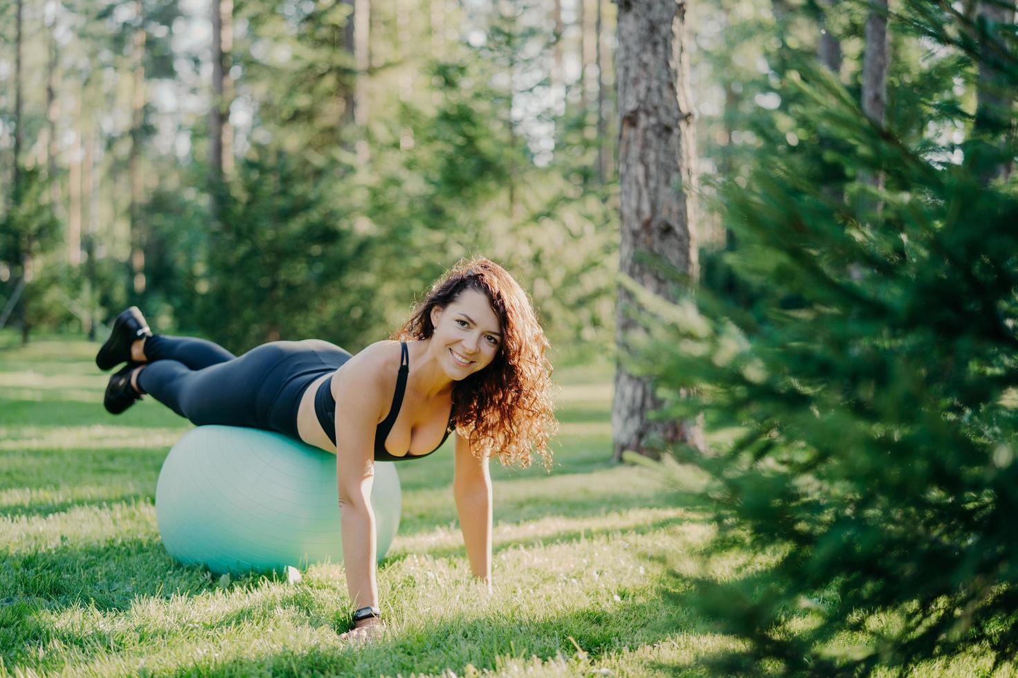 stile di vita attivo fitness e concetto di cura del corpo. adattare la giovane donna bruna soddisfatta indossa esercizi di abbigliamento sportivo con palla fitness pone nella foresta sull'erba verde. sportivi. esercizio di pilates foto