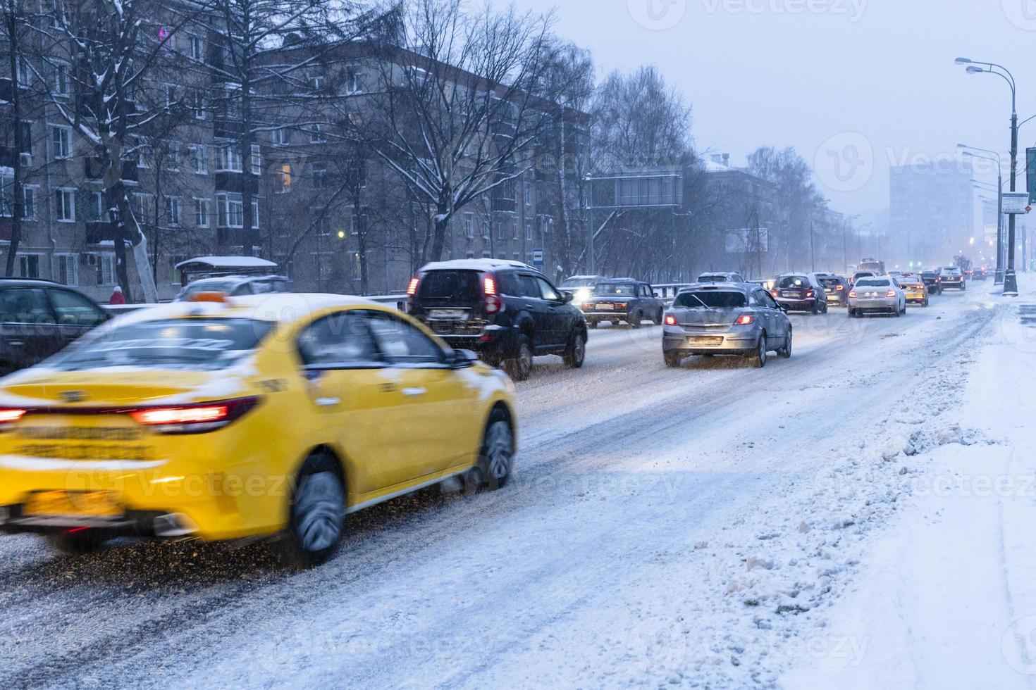 le auto guidano su una strada cittadina innevata nel crepuscolo invernale blu foto