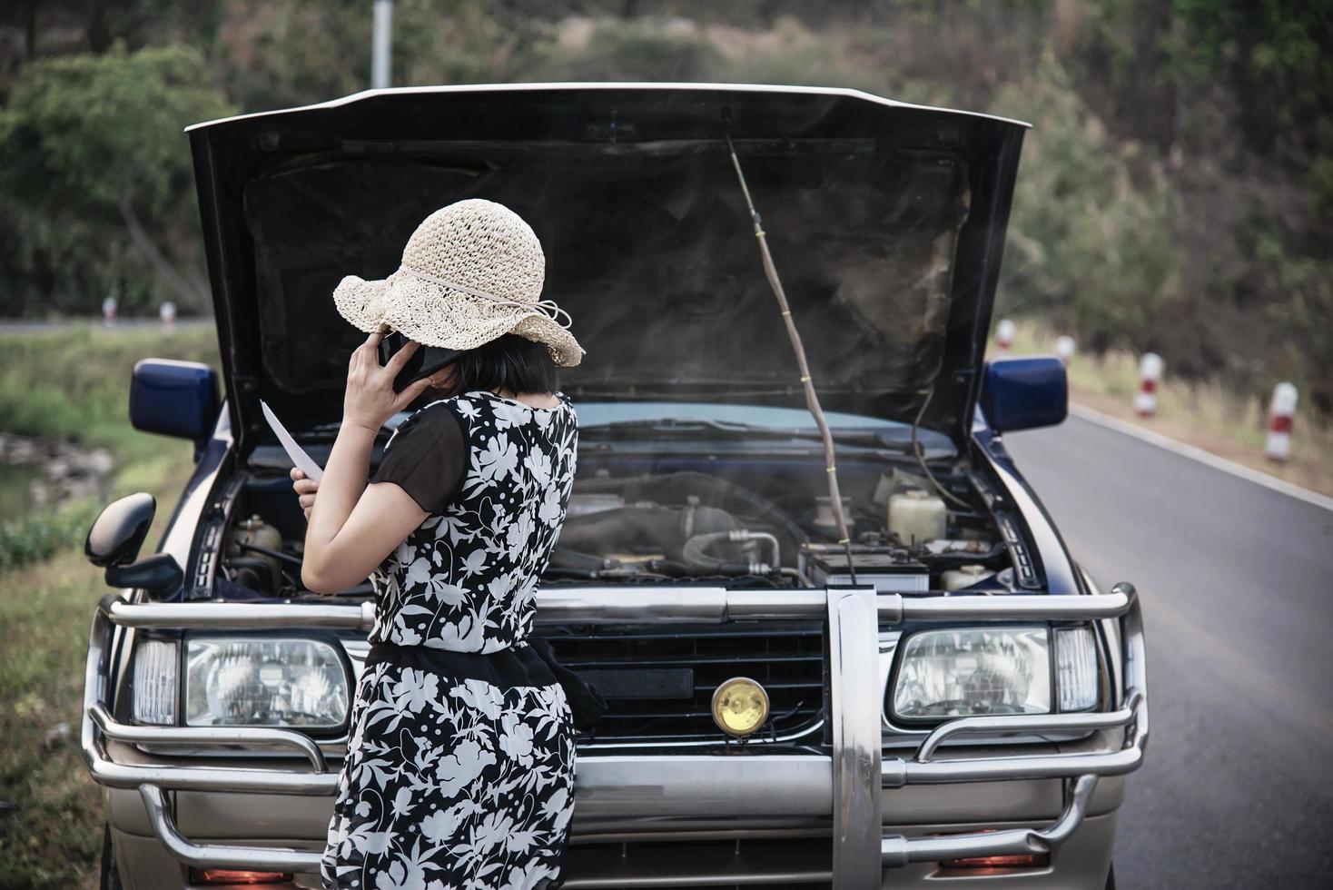 donna asiatica che chiama il riparatore o il personale assicurativo per risolvere un problema al motore di un'auto su una strada locale - persone con problemi di trasporto dell'auto concetto foto