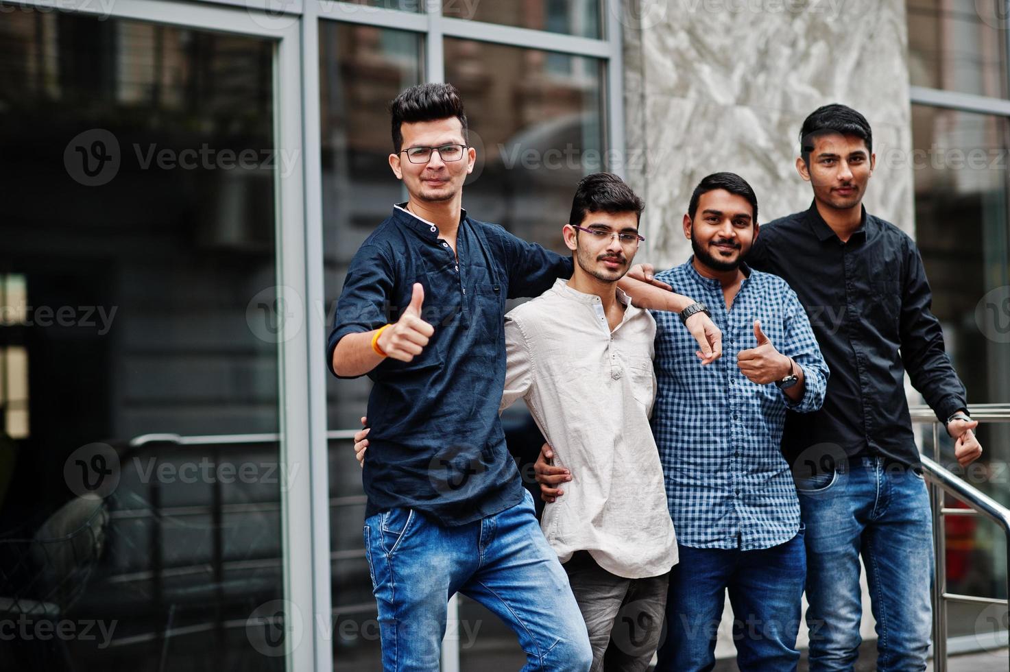 gruppo di quattro uomini indiani, indossare abiti casual, poste all'aperto in strada dell'india. mostra il pollice in su. foto