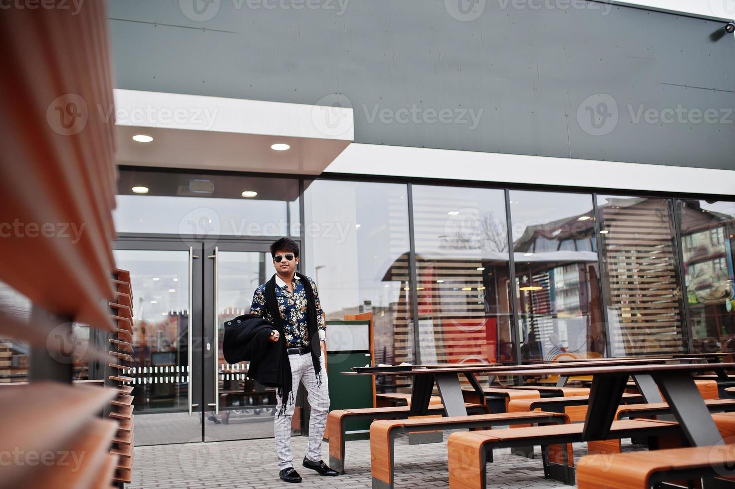 l'uomo indiano alla moda attraente e bello indossa camicia e occhiali da sole in piedi sulla terrazza del moderno lounge cafe durante la sua pausa di lavoro. foto