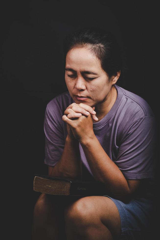 la mano della donna cristiana sulla Bibbia è pregare e adorare per ringraziare dio in chiesa con sfondo nero, concetto di fede, spiritualità e religione foto