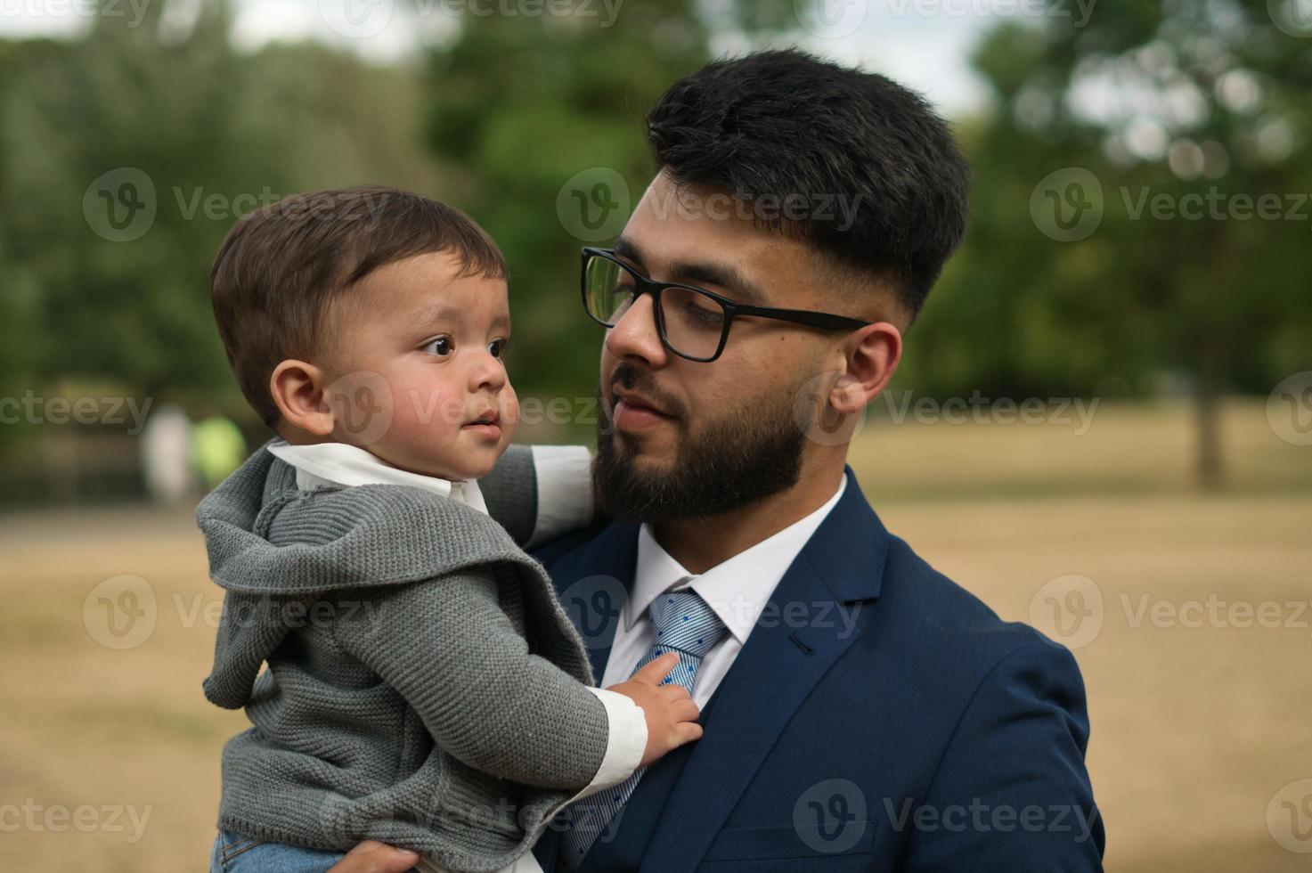 il padre pakistano asiatico tiene in braccio il suo bambino di 11 mesi nel parco locale foto