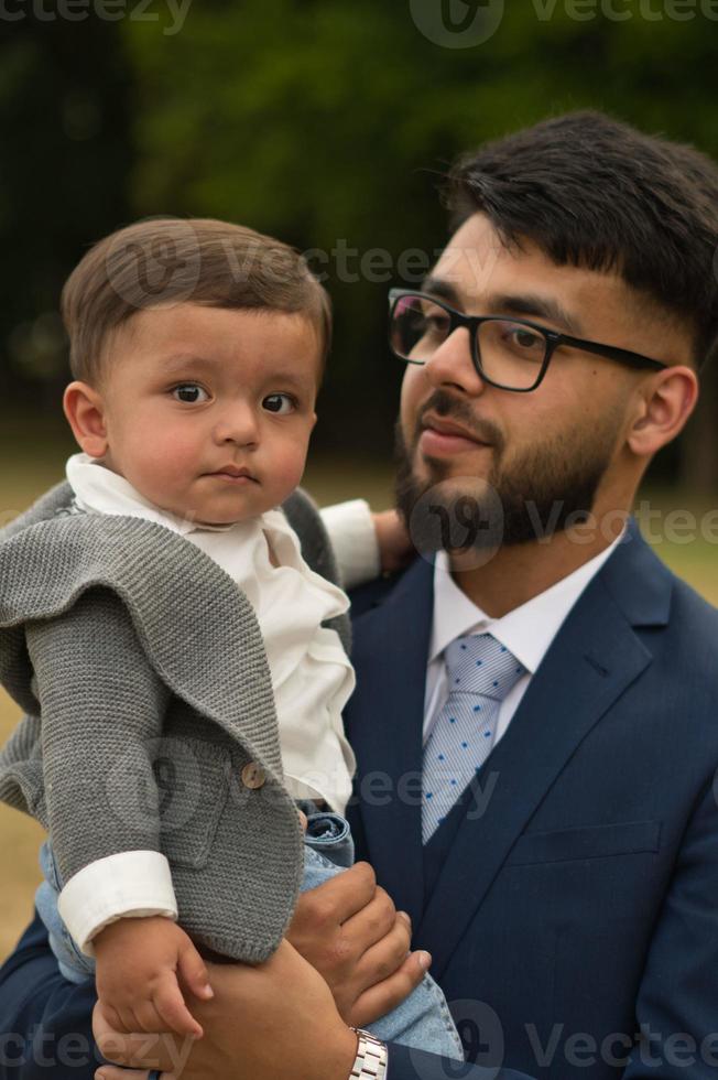 il padre pakistano asiatico tiene in braccio il suo bambino di 11 mesi nel parco locale foto