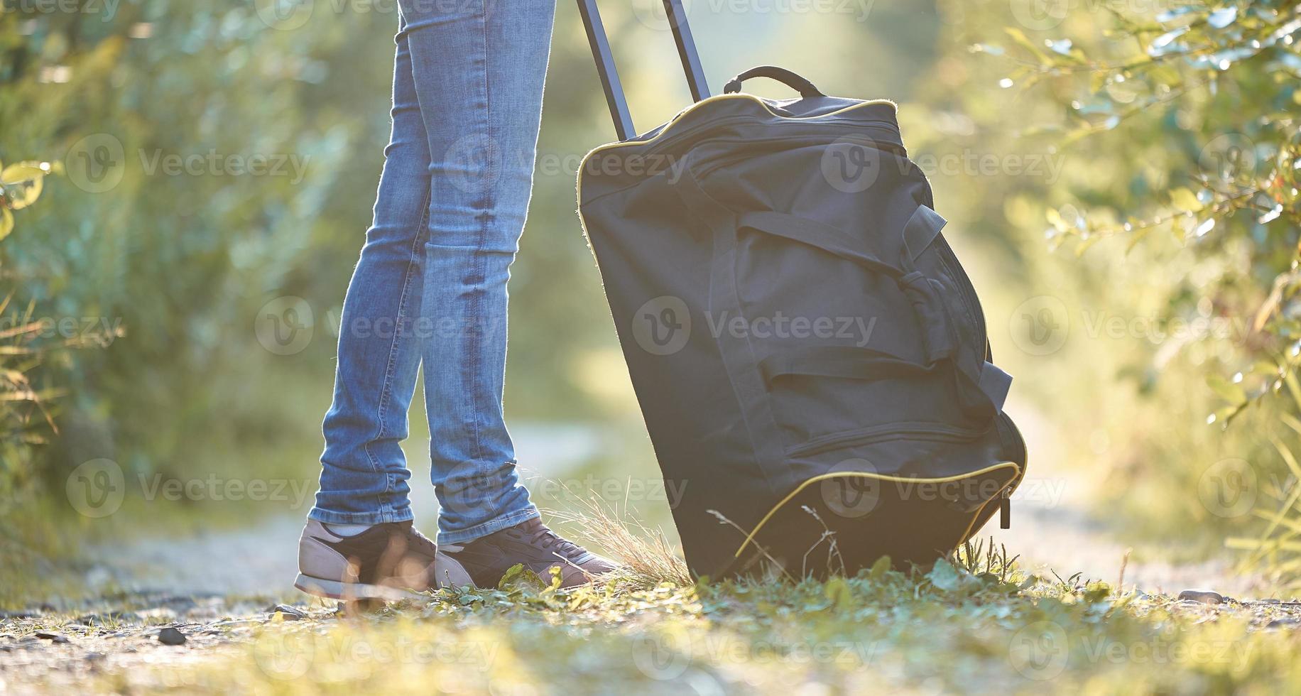 gambe da donna e una borsa da viaggio nera sulla strada del villaggio. foto