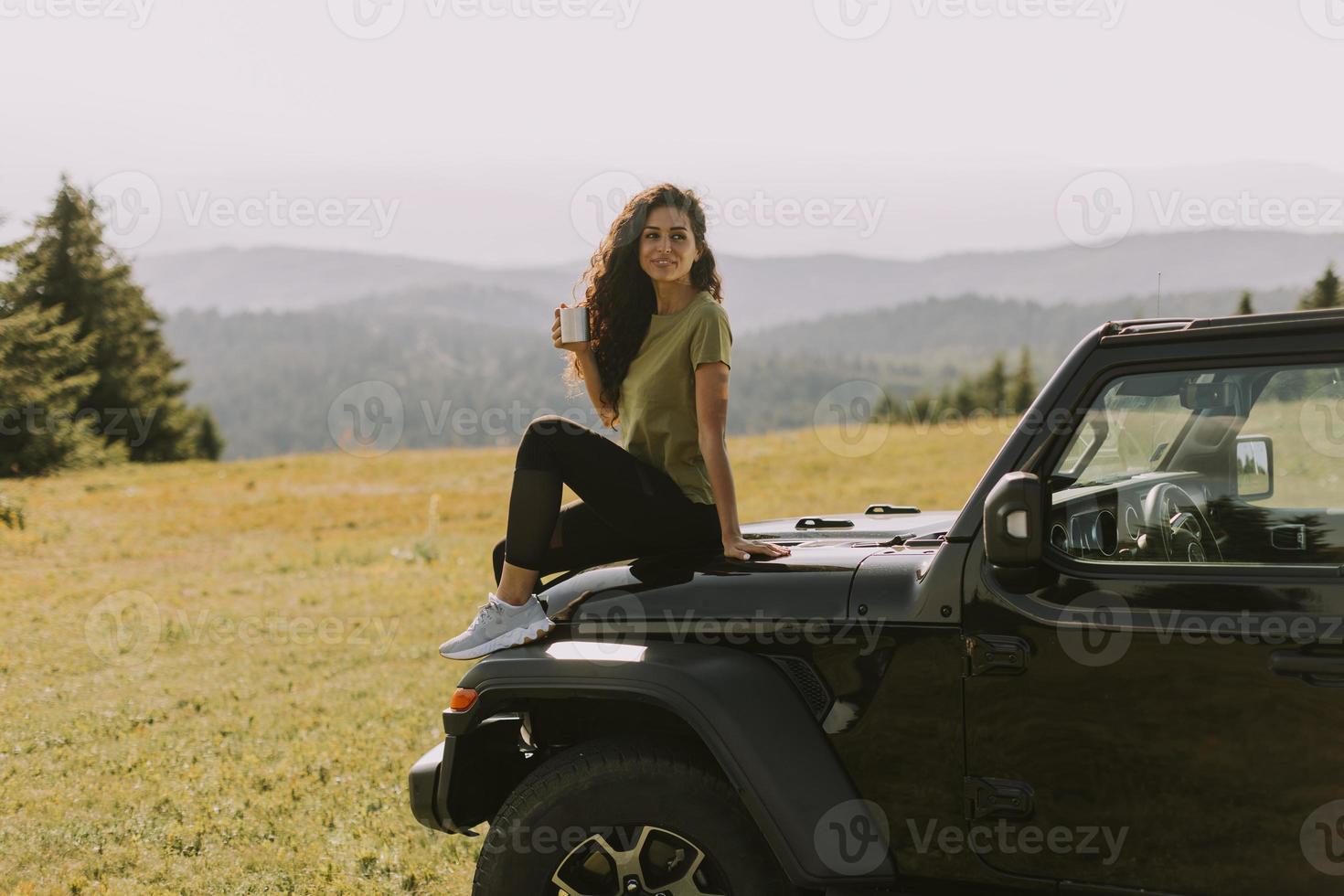 giovane donna che si rilassa su un cofano di un veicolo fuoristrada in campagna foto