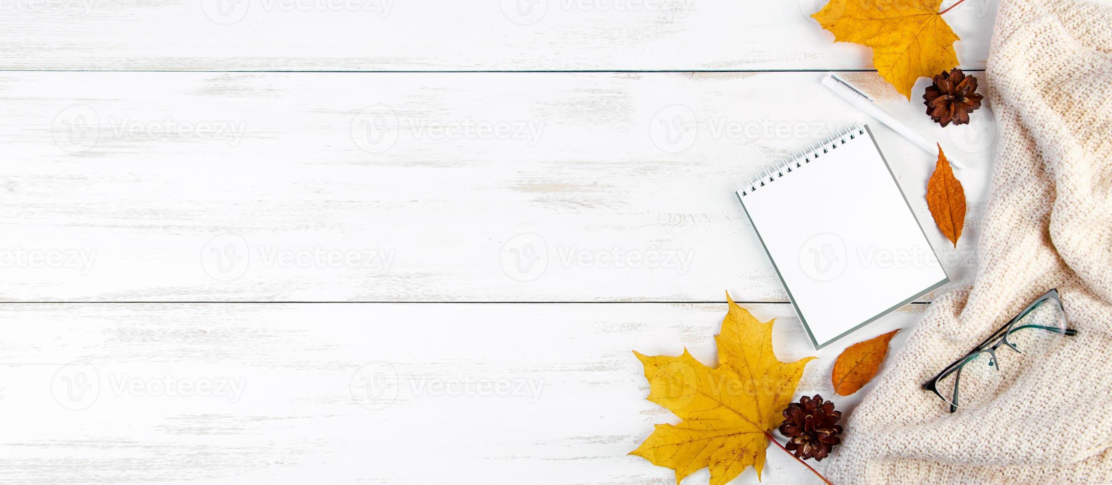 Ciao autunno. foglie gialle, blocco note e bicchieri. spazio di lavoro elegante. composizione piatta su fondo di legno bianco. foto