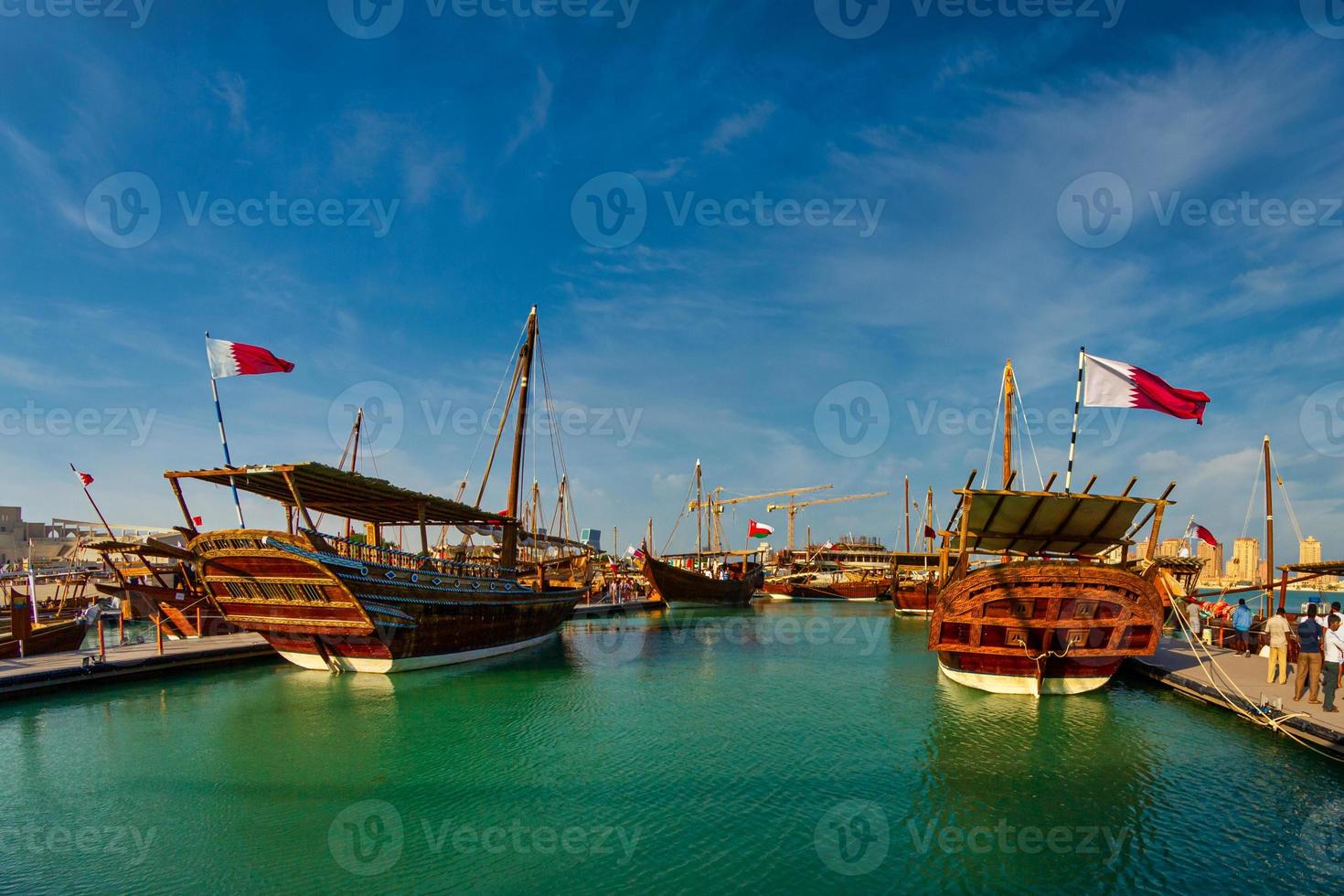 barche tradizionali di legno, dhow, in spiaggia di katara, vista diurna di doha qatar con bandiera del qatar e nuvole in cielo foto