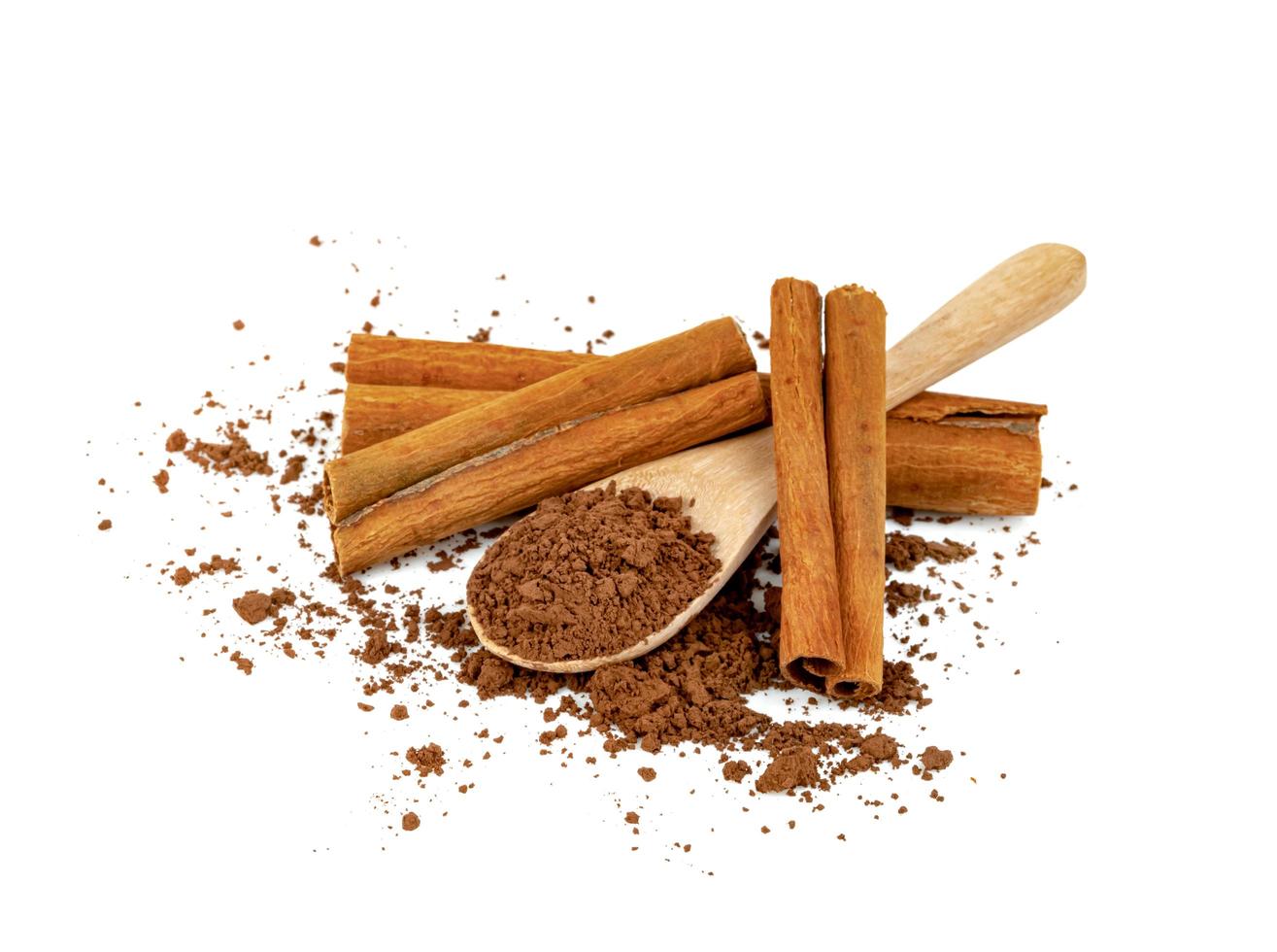 cacao in polvere e bastoncini di cannella con cucchiaio di legno isolato su sfondo bianco foto