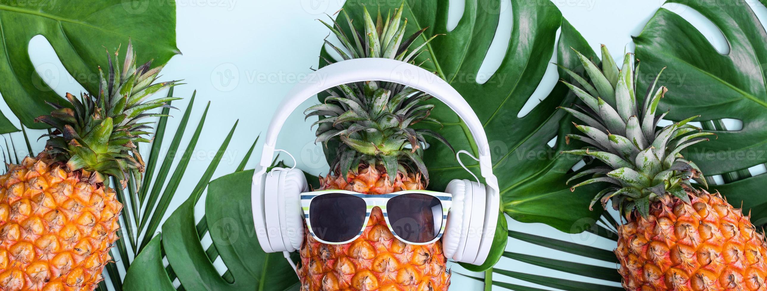 divertente ananas con cuffie bianche, concetto di ascolto di musica, isolato su sfondo colorato con foglie di palma tropicali, vista dall'alto, design piatto. foto