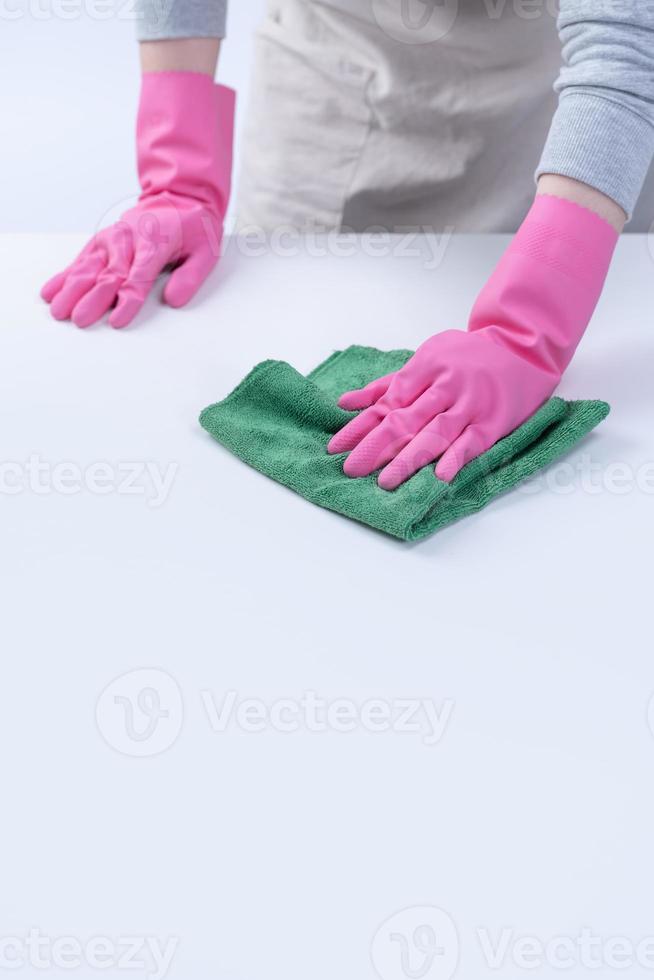 giovane donna governante in grembiule indossa guanti rosa per pulire il tavolo, concetto di prevenzione dell'infezione da virus, servizio di pulizia, primo piano. foto