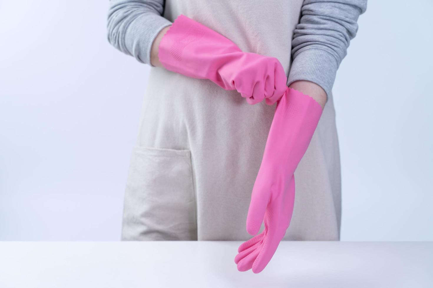 giovane donna governante in grembiule indossa guanti rosa per pulire il tavolo, concetto di prevenzione dell'infezione da virus, servizio di pulizia, primo piano. foto