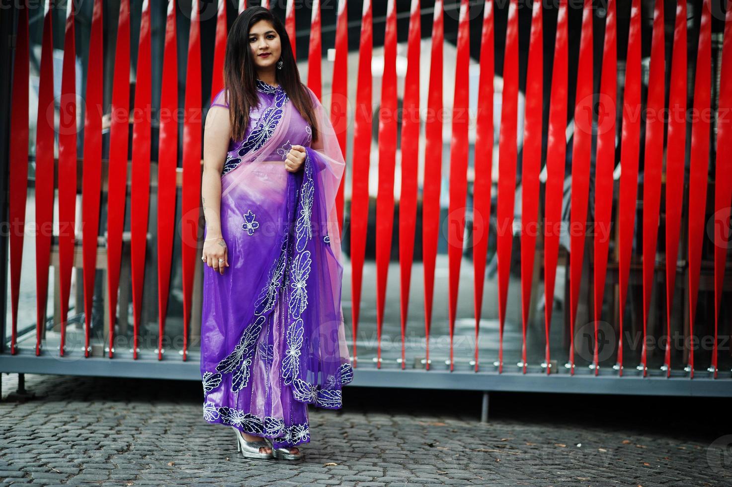 ragazza indù indiana al tradizionale saree viola poste in strada su sfondo rosso. foto