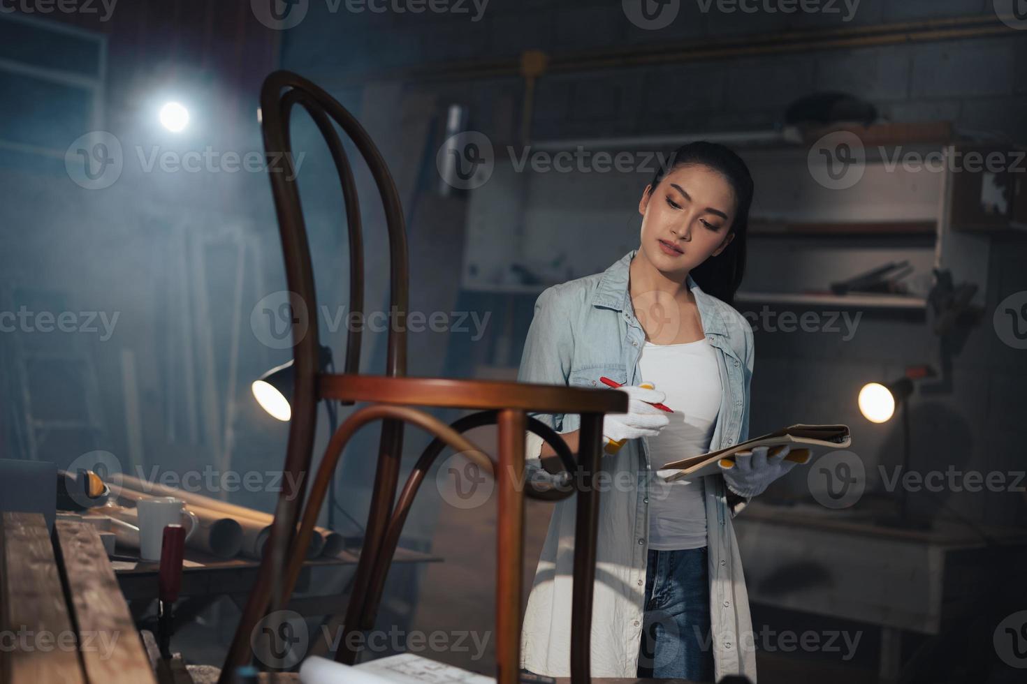 il giovane falegname asiatico di mobili di design donna utilizza un metro a nastro per misurare la sedia sul banco di lavoro nel laboratorio di falegnameria di falegnameria. foto
