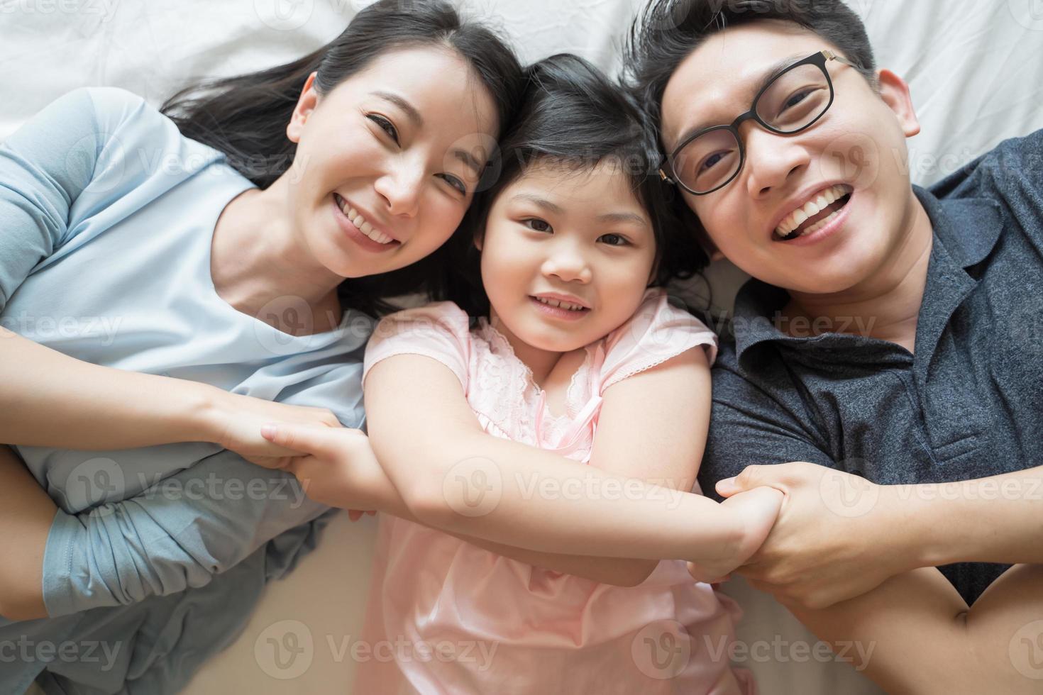 ritratto di felice famiglia asiatica sdraiata sul letto e guardando in alto e tenendosi per mano foto