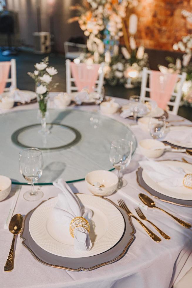 composizione floreale per il matrimonio estivo, fatta di rose e rami verdi su un tavolo da pranzo nel ristorante. , bicchieri e piatti nel ristorante all'aperto in una giornata ventosa con effetto grana della pellicola foto