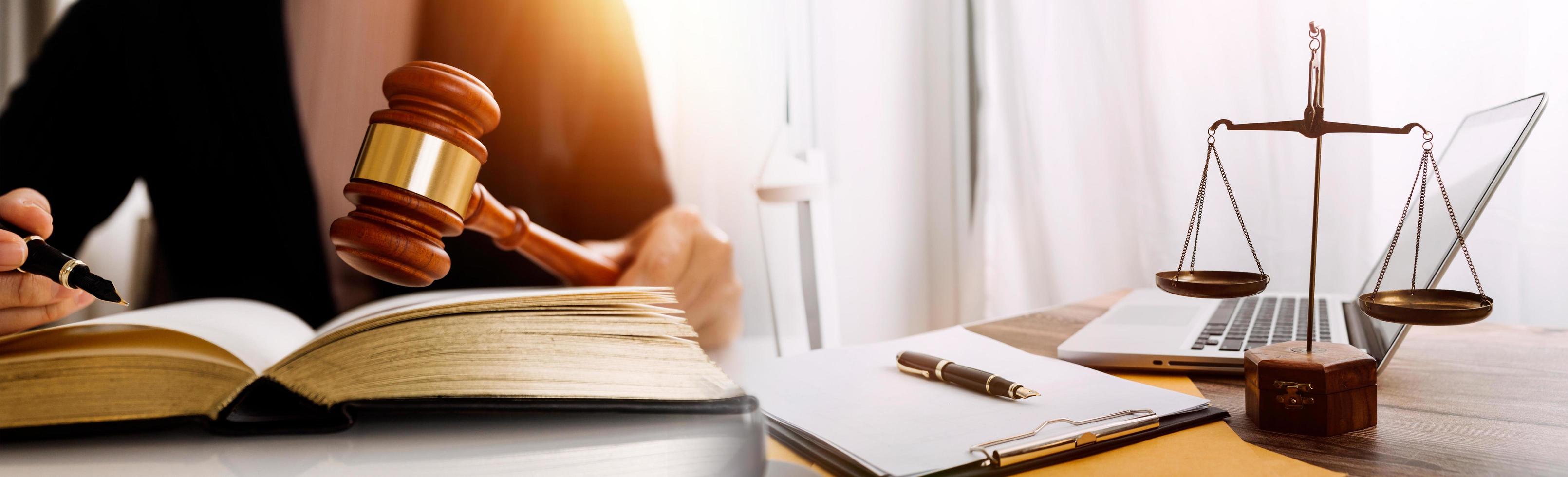 concetto di giustizia e diritto. giudice maschio in un'aula di tribunale con il martelletto, lavorando con computer e tastiera docking, occhiali, sul tavolo alla luce del mattino foto