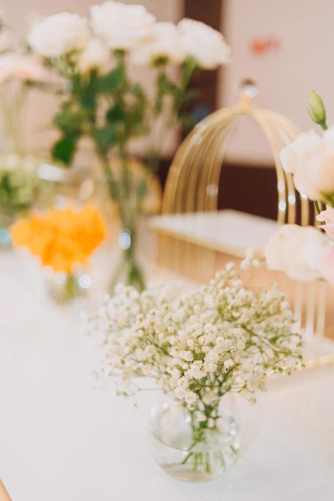 composizione floreale per il matrimonio estivo, fatta di rose e rami verdi su un tavolo da pranzo nel ristorante. , bicchieri e piatti nel ristorante all'aperto in una giornata ventosa con effetto grana della pellicola foto