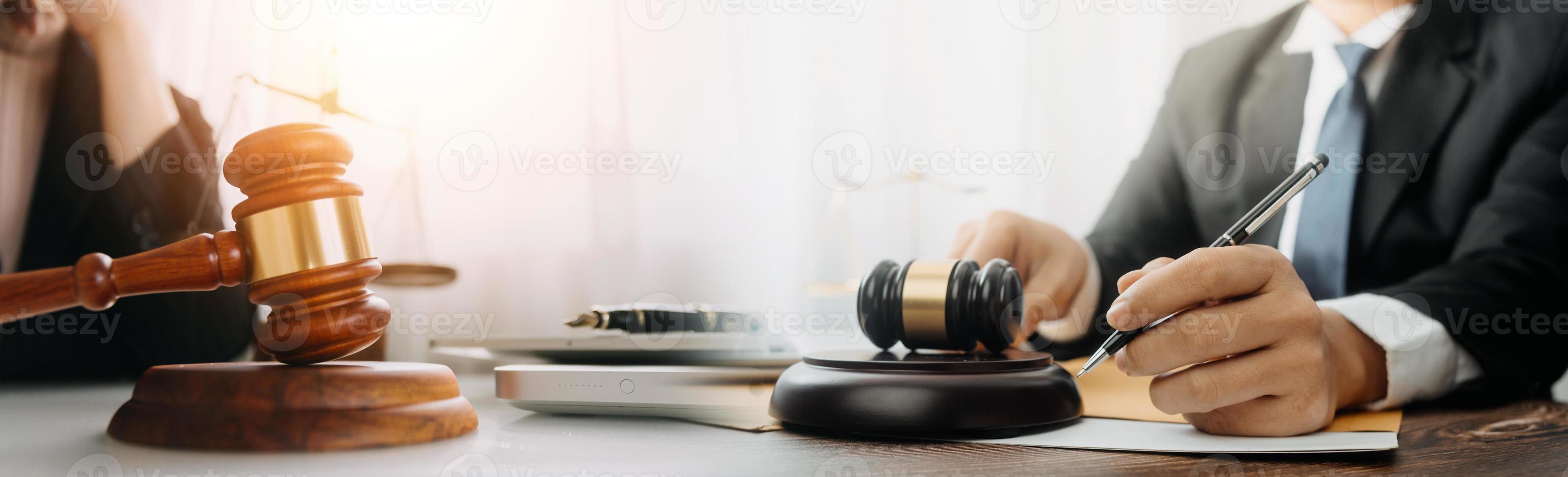 concetto di giustizia e diritto. giudice maschio in un'aula di tribunale con il martelletto, lavorando con computer e tastiera docking, occhiali, sul tavolo alla luce del mattino foto