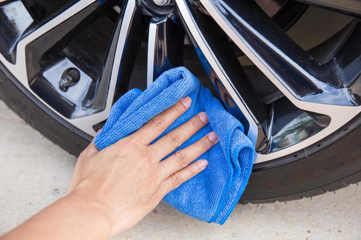 mano con panno in microfibra blu per la pulizia della ruota dell'auto. foto