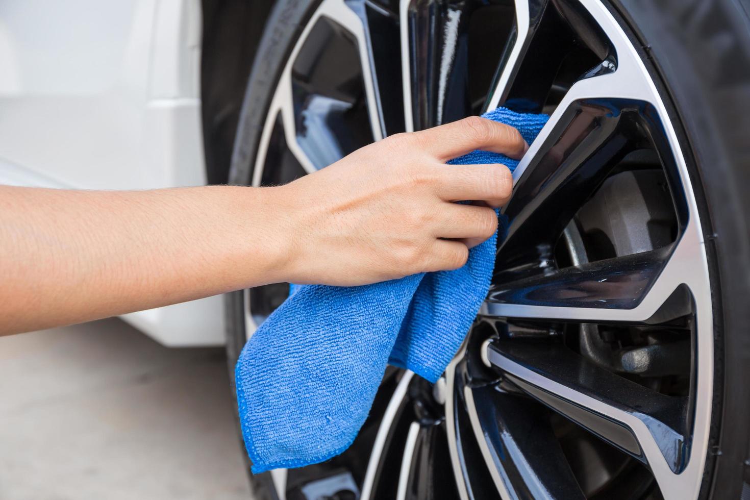 mano con panno in microfibra blu per la pulizia della ruota dell'auto. foto