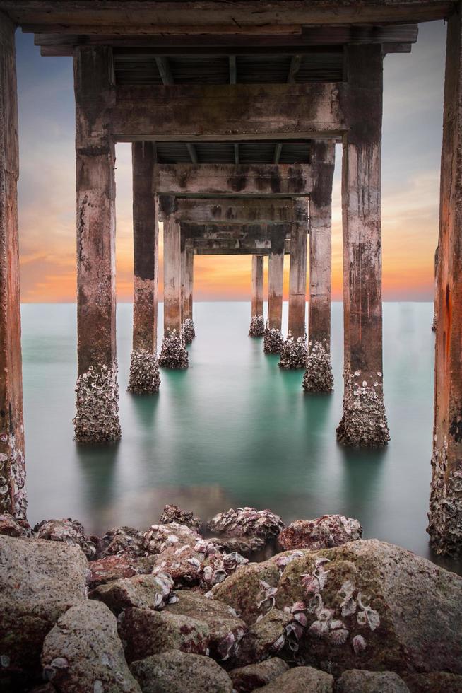 buio di sotto i tralicci di una lunga spiaggia del molo del molo che si affaccia sul mare al tramonto o al crepuscolo a khao laem ya mu ko samet national park rayong, thailandia. scatto a lunga esposizione di paesaggio marino foto