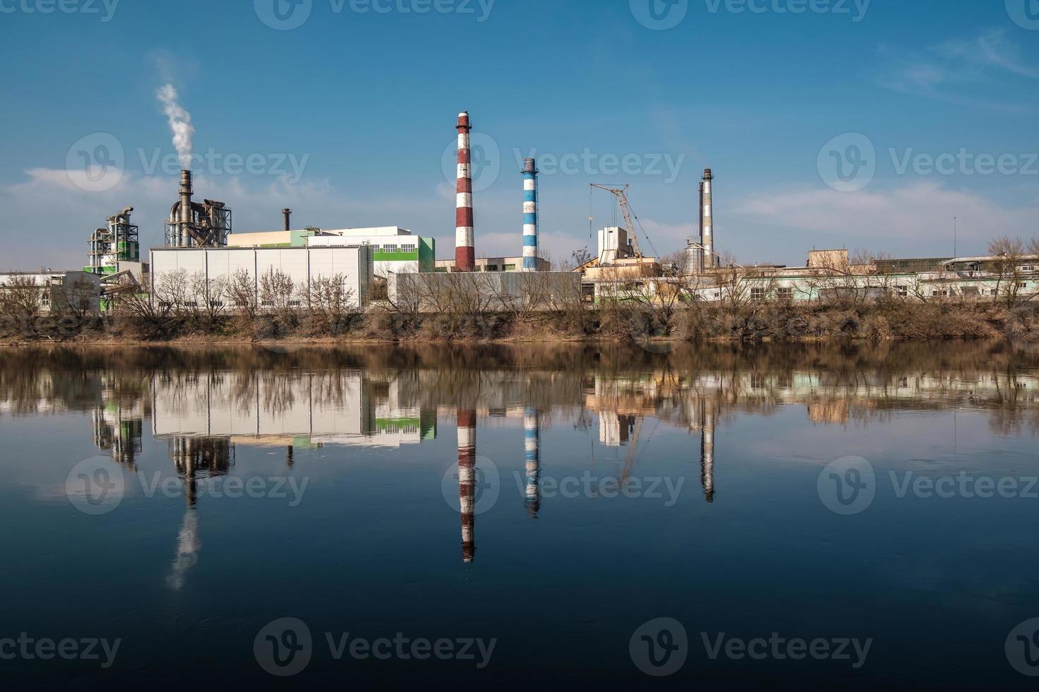 tubi della segheria dell'impianto di impresa di lavorazione del legno vicino al fiume. concetto di inquinamento atmosferico. paesaggio industriale inquinamento ambientale rifiuti di centrale termica foto