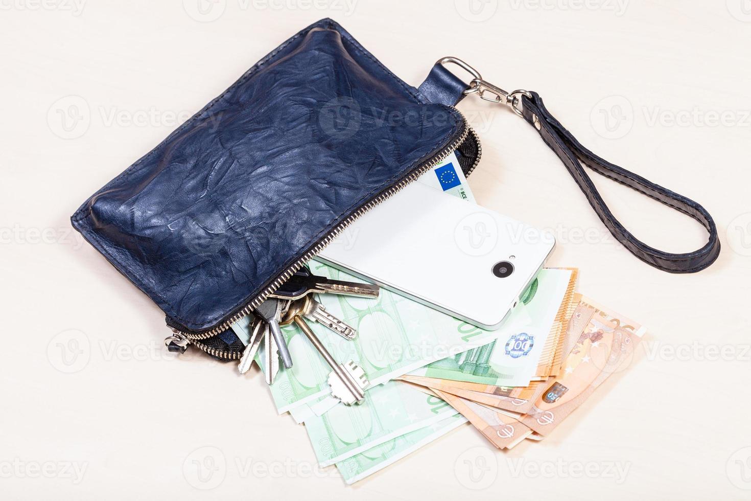 pochette con telefono, chiavi e tanti euro sul tavolo foto