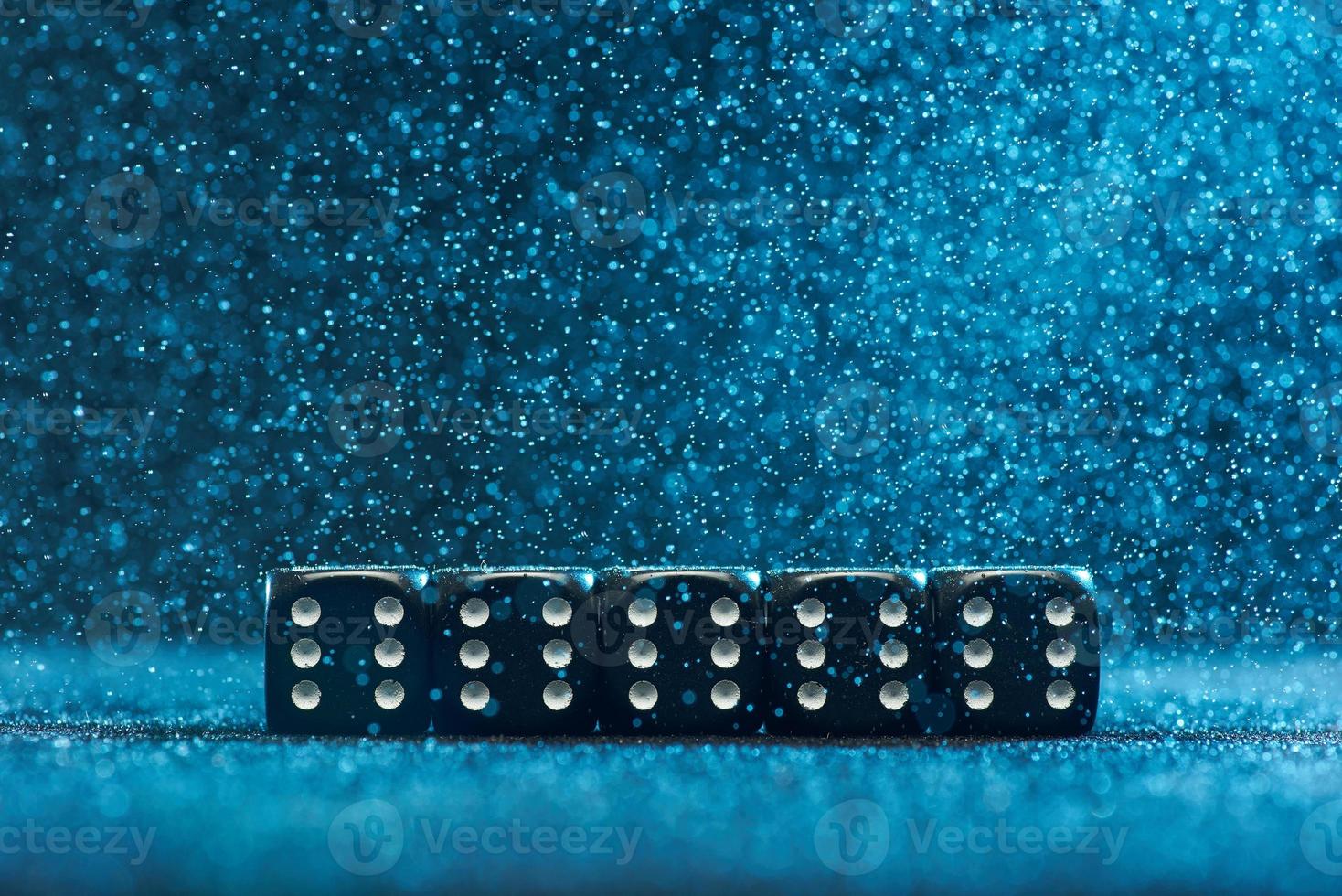 i cubi di gioco sono uno accanto all'altro. cinque cubi neri identici su sfondo blu. foto con bokeh.
