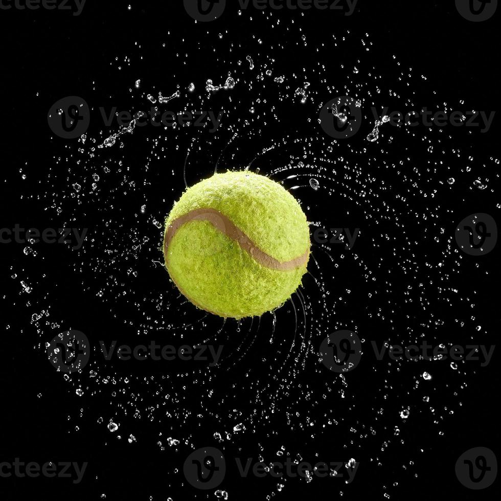 palla da tennis che gira velocemente spruzzi d'acqua gocce in un cerchio su sfondo nero. foto