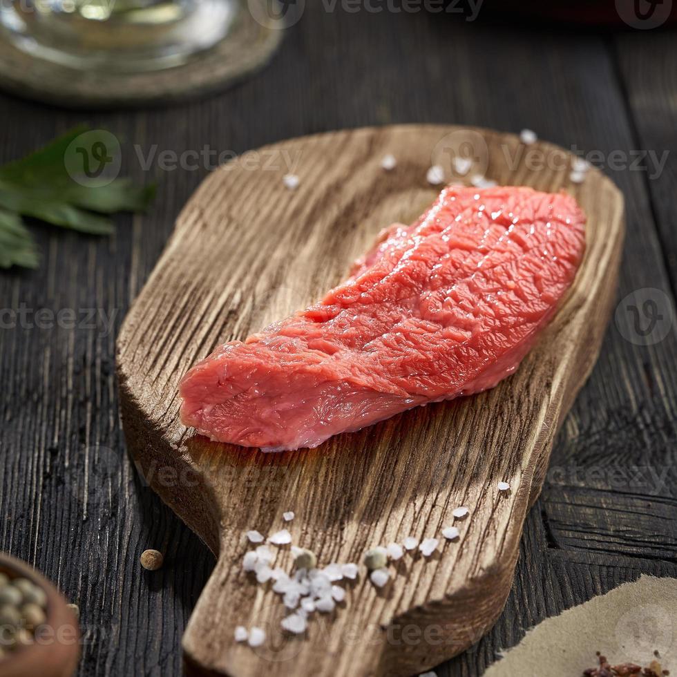 pezzo di manzo fresco crudo e sale grosso su un vecchio tagliere. sfondo tavolo in legno scuro. foto