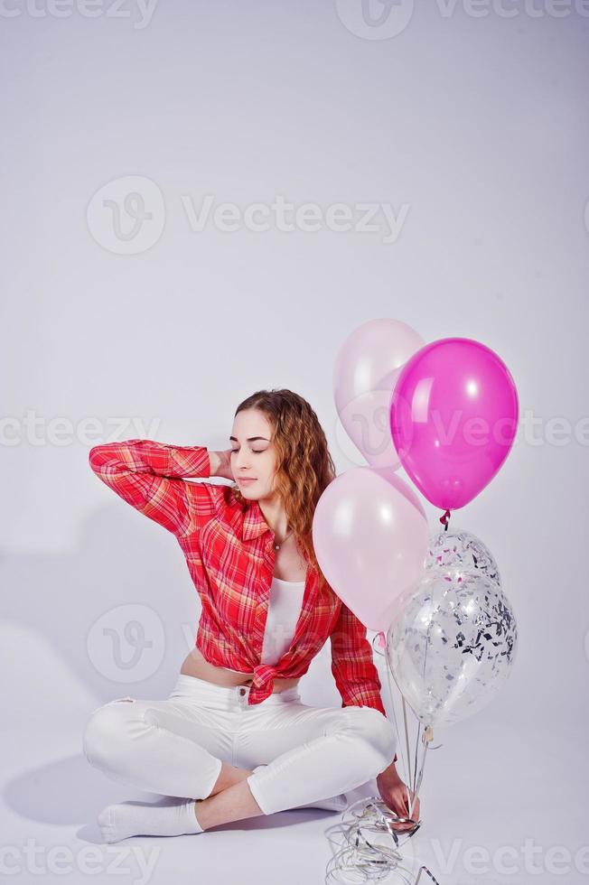 giovane ragazza in camicia rossa a quadri e pantaloni bianchi con palloncini su sfondo bianco in studio. foto