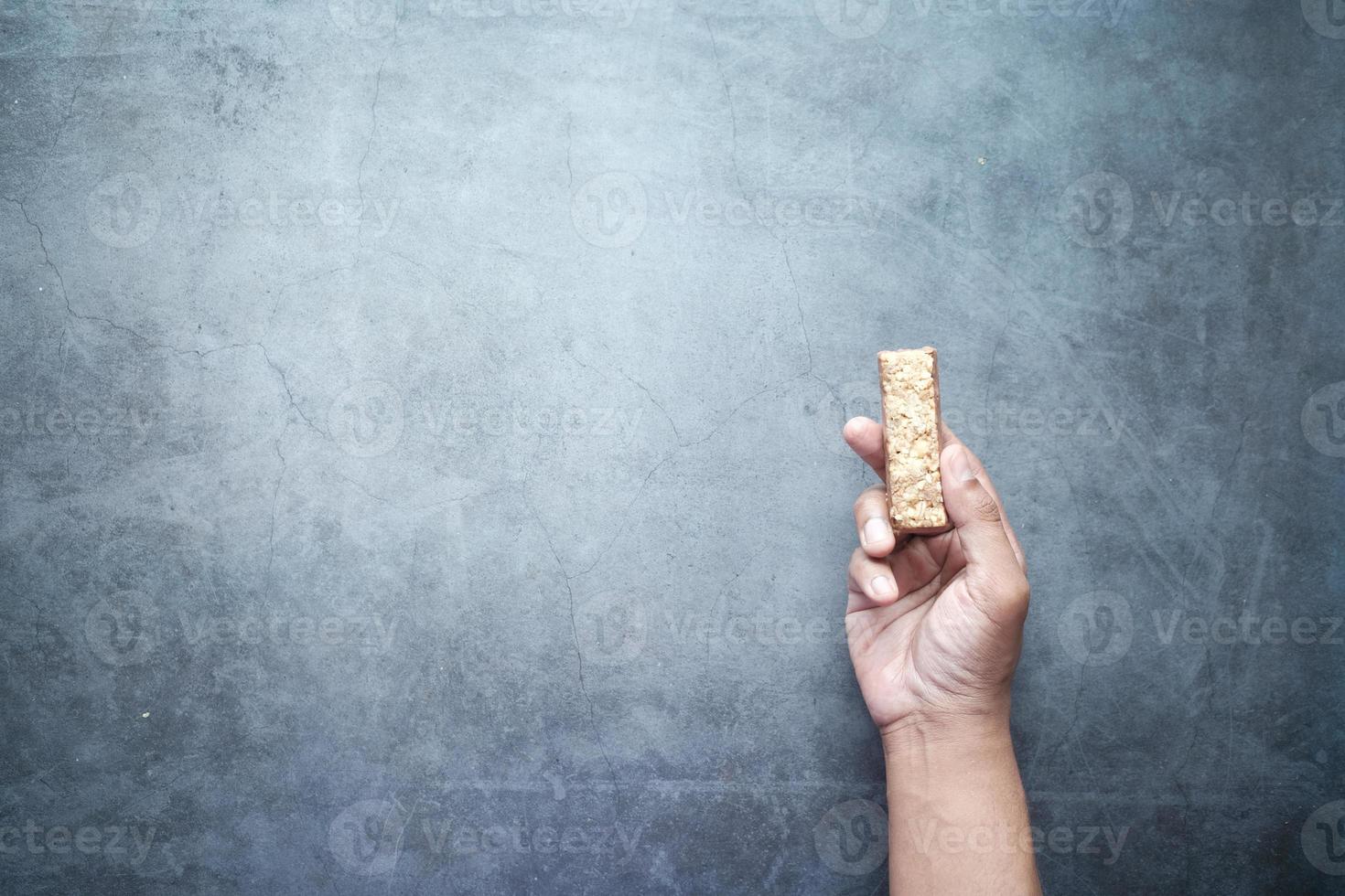 con in mano una barretta proteica di mandorle, uvetta e avena su sfondo nero foto