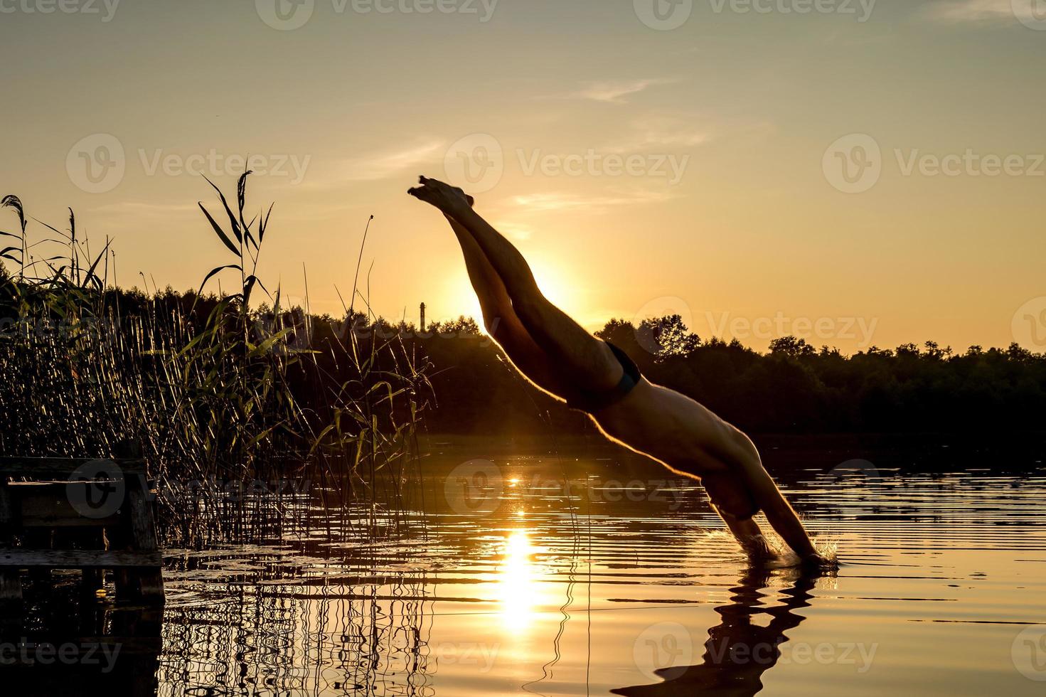 l'uomo si tuffa nell'acqua del lago al tramonto foto