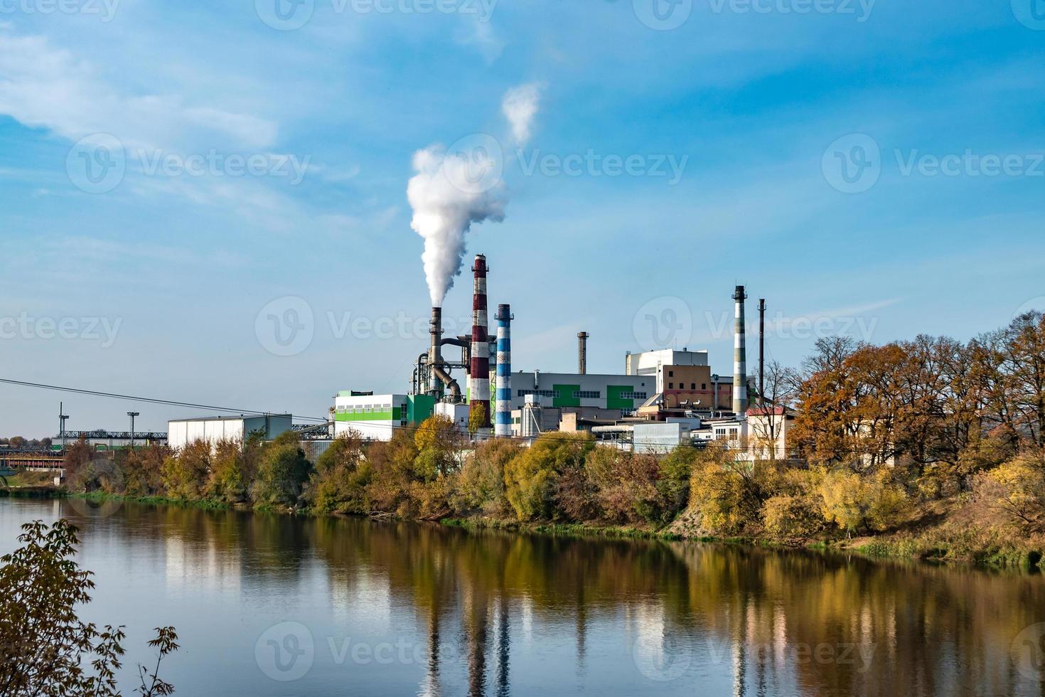 tubi della segheria dell'impianto di impresa di lavorazione del legno vicino al fiume. concetto di inquinamento atmosferico. paesaggio industriale inquinamento ambientale rifiuti di centrale termica foto