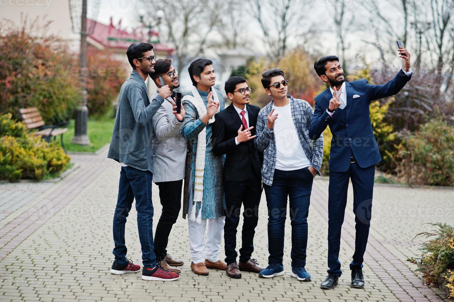 un gruppo di sei uomini indiani del sud asiatico in abiti tradizionali, casual e da lavoro in piedi e facendo selfie insieme al telefono cellulare. foto