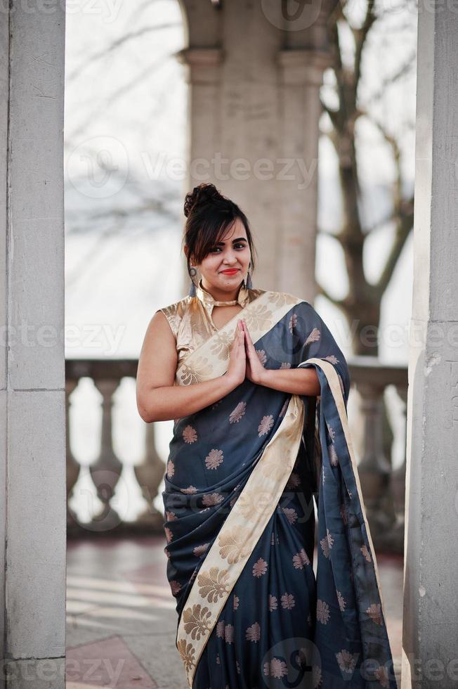 elegante bruna ragazza indiana del sud asiatico in saree in piedi sotto l'arco e mostra il segno delle mani di namaste. foto