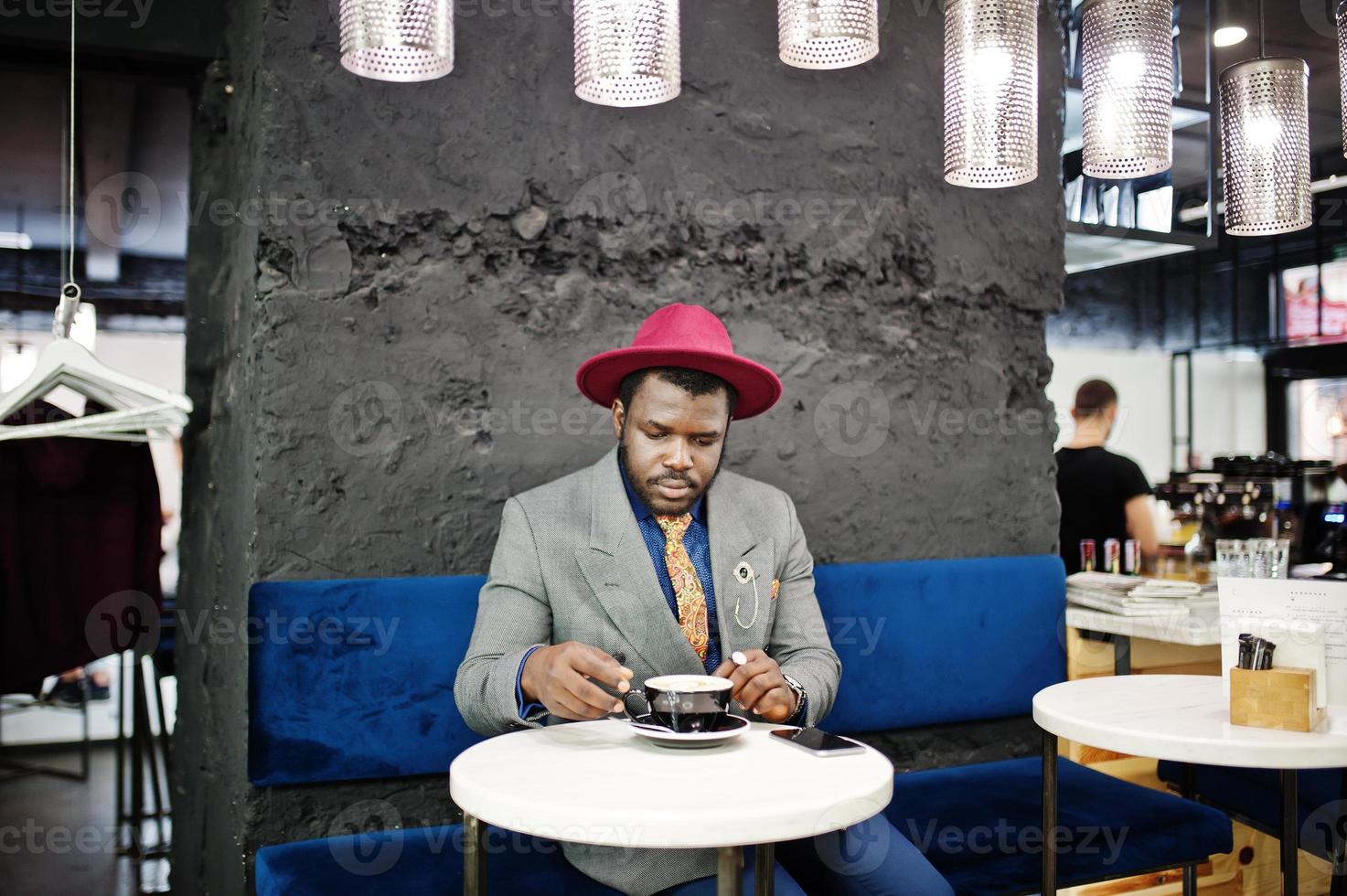 elegante uomo afroamericano modello in giacca grigia cravatta e cappello rosso bere caffè al bar. foto